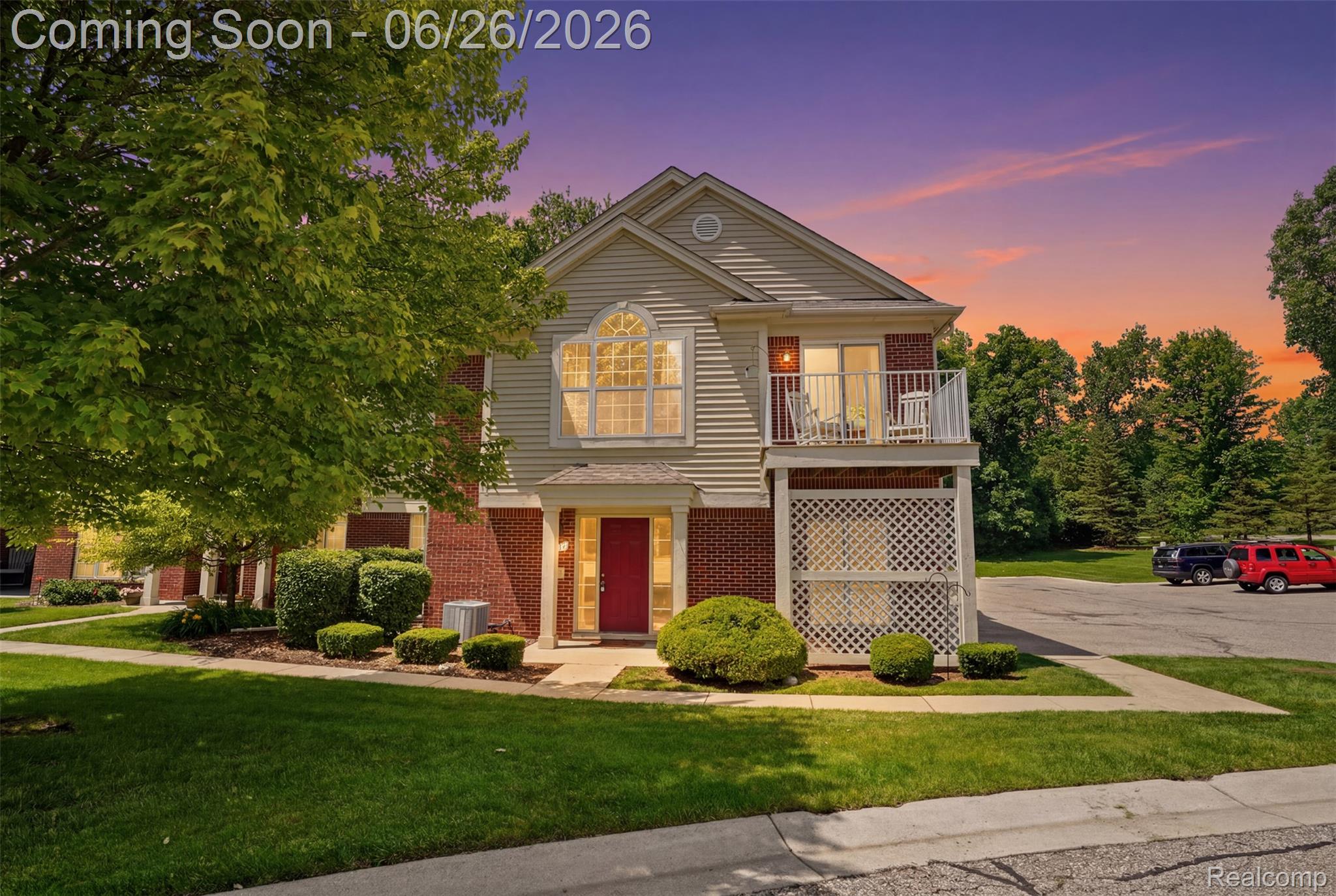 Two-story residence featuring brick and siding facade, a red entry door, an upper-level balcony with white railing, a ground-level lattice privacy screen, and manicured landscaping