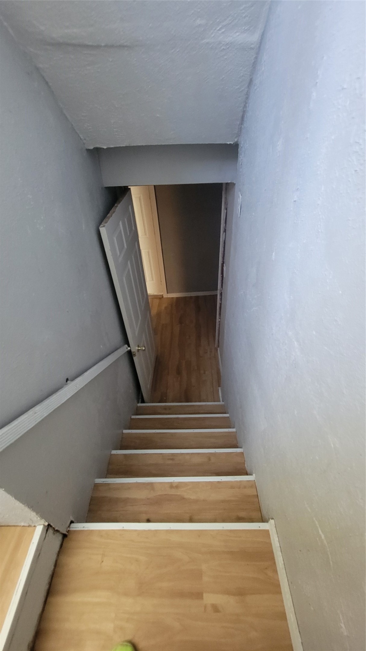 12018 Sandpiper Road Angleton, TX 77515 - Photo 21 of 48 This photo shows a narrow staircase with wooden steps leading down to a lower level. The walls are painted light gray, and there's a white door at the bottom opening into a room with similar flooring.
