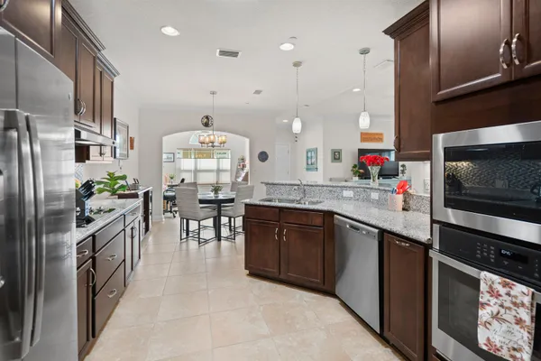 a kitchen with stainless steel appliances granite countertop a refrigerator a sink dishwasher a stove and a dining table with wooden floor