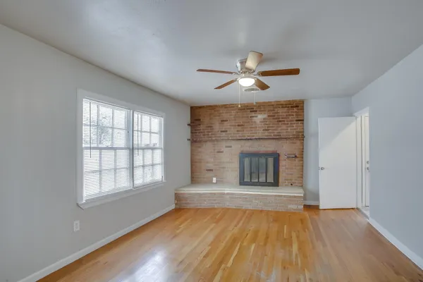 an empty room with wooden floor fan and windows