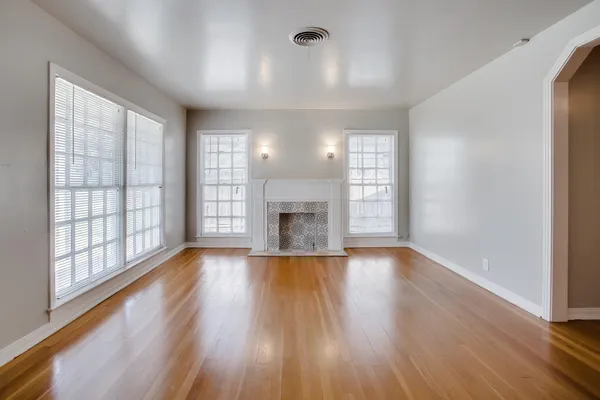 an empty room with wooden floor fireplace and windows