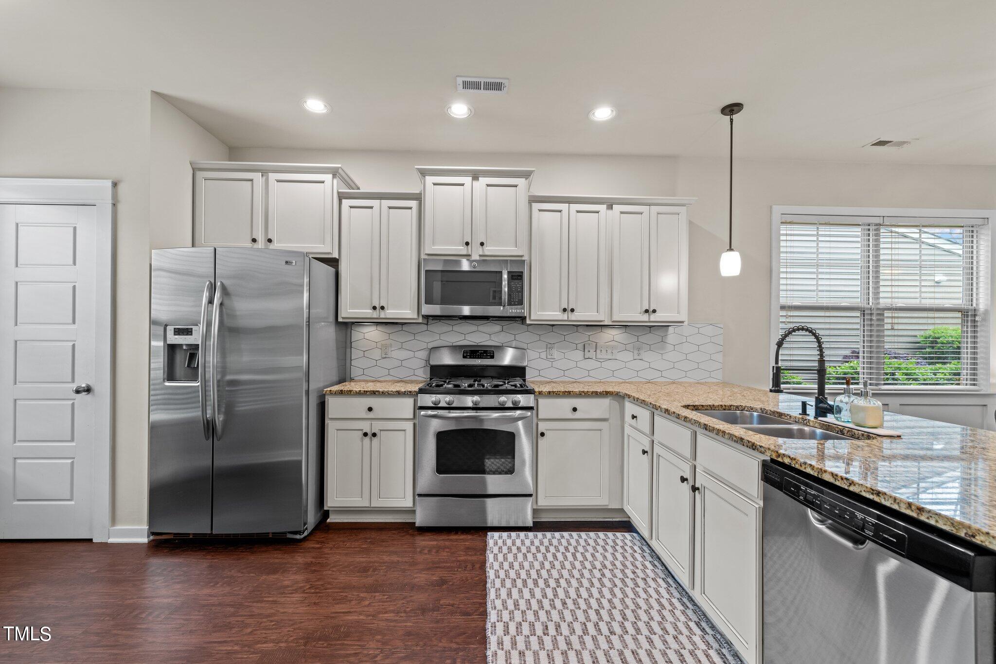 7837 Allscott Way Raleigh, NC 27612 - Photo 3 of 17 a kitchen with stainless steel appliances granite countertop a refrigerator a sink a stove and white cabinets with wooden floor