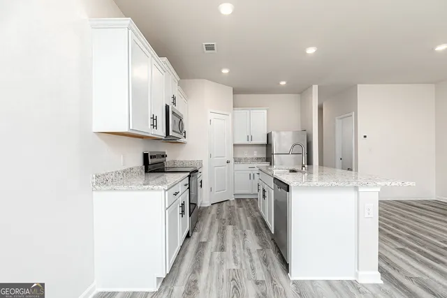 a kitchen with stainless steel appliances granite countertop a stove top oven a sink a refrigerator and white cabinets with wooden floor