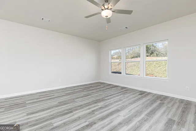 an empty room with wooden floor fan and windows
