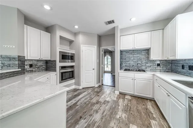 a kitchen with stainless steel appliances kitchen island granite countertop a stove top oven a sink and white cabinets