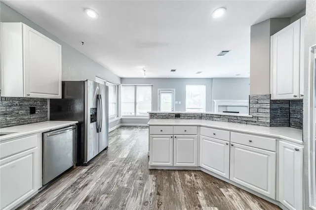 a kitchen with stainless steel appliances granite countertop a stove a sink dishwasher a refrigerator and white cabinets with wooden floor