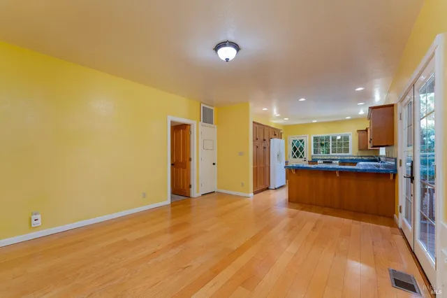 a living room with stainless steel appliances dining table wooden floor and kitchen view
