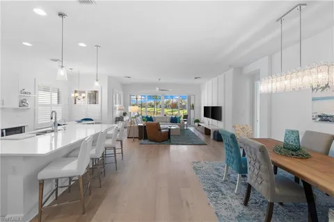 a kitchen with stainless steel appliances kitchen island granite countertop a dining table chairs refrigerator sink and cabinets