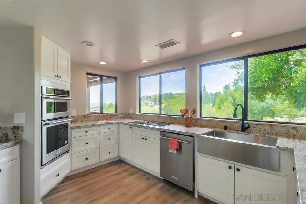 1660 Grove Road El Cajon, CA 92020 - Photo 9 of 44 a kitchen with stainless steel appliances granite countertop a stove a sink and white cabinets with wooden floor