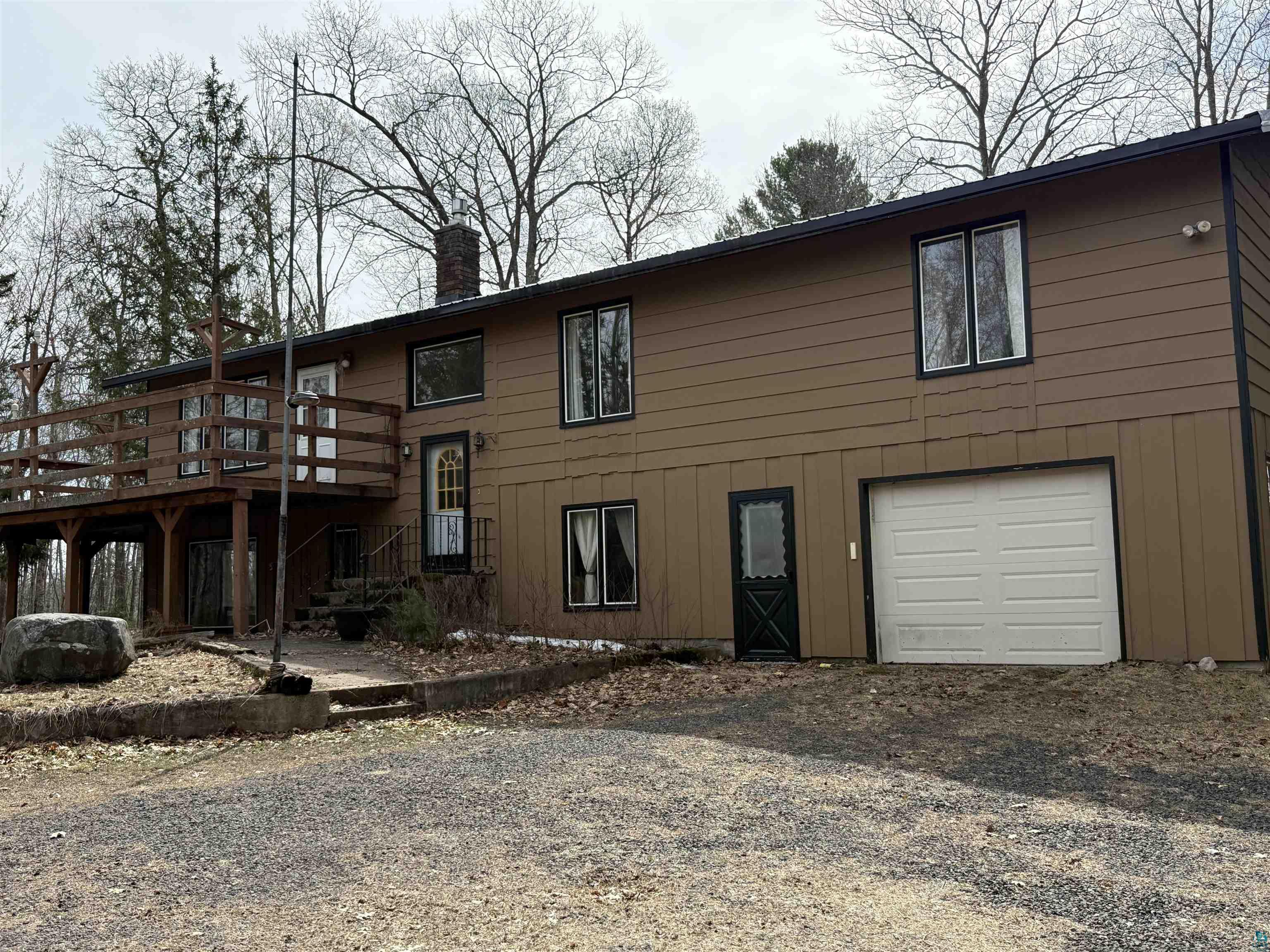 Two-story property with brown siding and black trim, featuring a prominent wood deck with railing