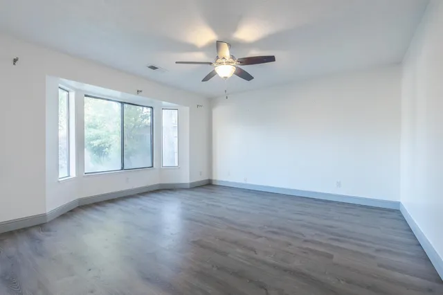 an empty room with wooden floor fan and windows