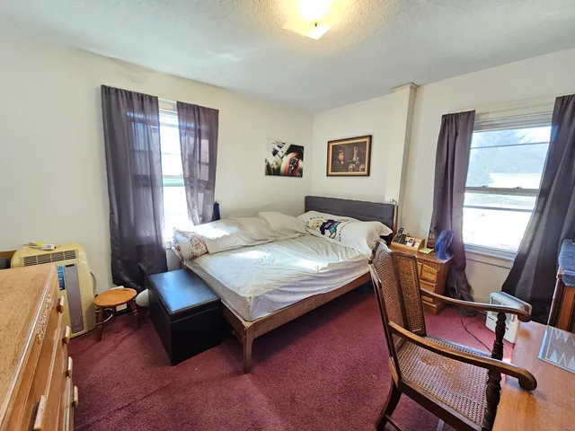 a bedroom with a bed a desk and chair with the wooden floor