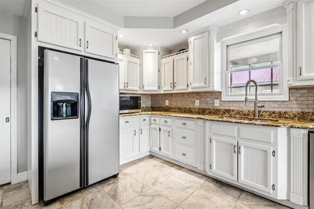 a kitchen with granite countertop a refrigerator sink and white cabinets