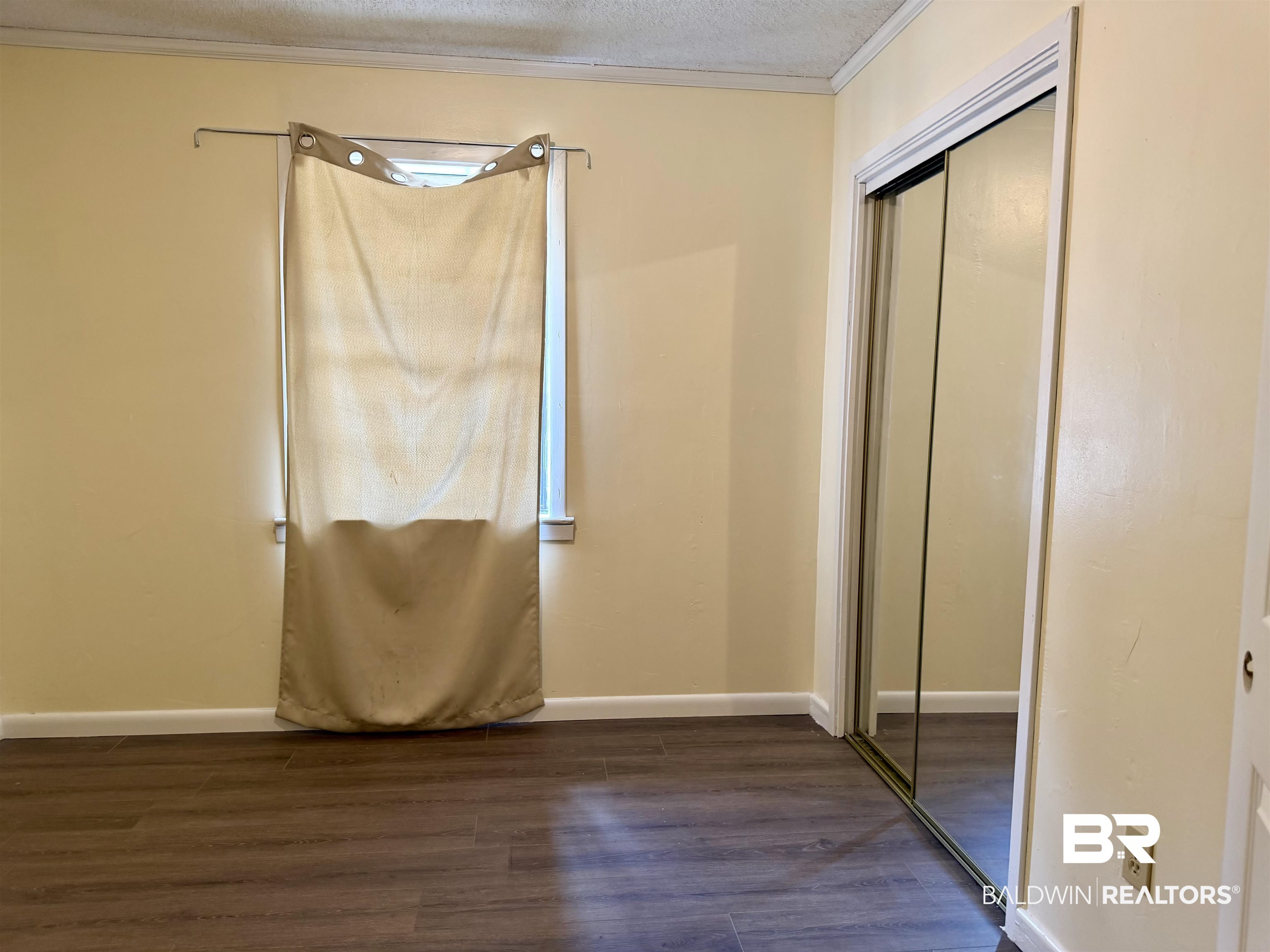 294 Wolf Log Road Flomaton, AL 36441 - Photo 10 of 14 Unfurnished bedroom with dark wood-style floors, a closet, ornamental molding, and a textured ceiling