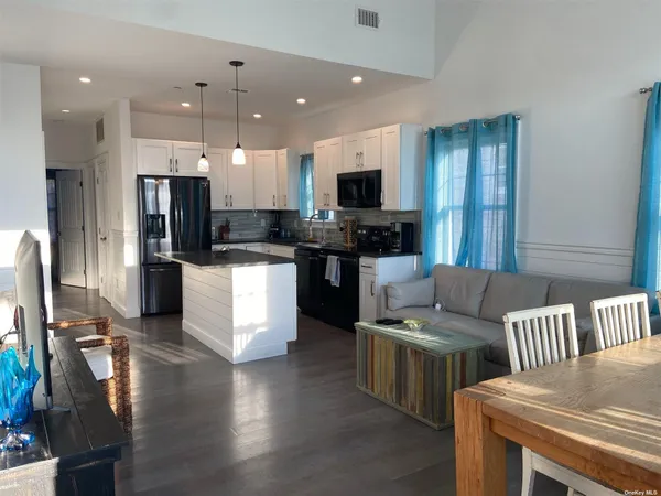 a kitchen with stainless steel appliances kitchen island granite countertop a refrigerator a stove a sink a microwave a dining table and chairs with wooden floor