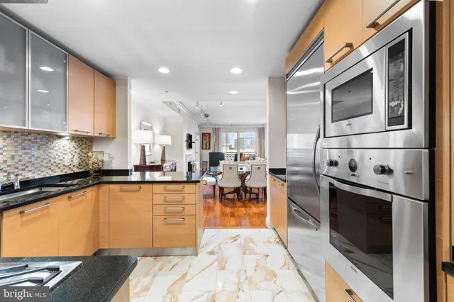 a kitchen with stainless steel appliances granite countertop a stove top oven a sink a dining table and chairs