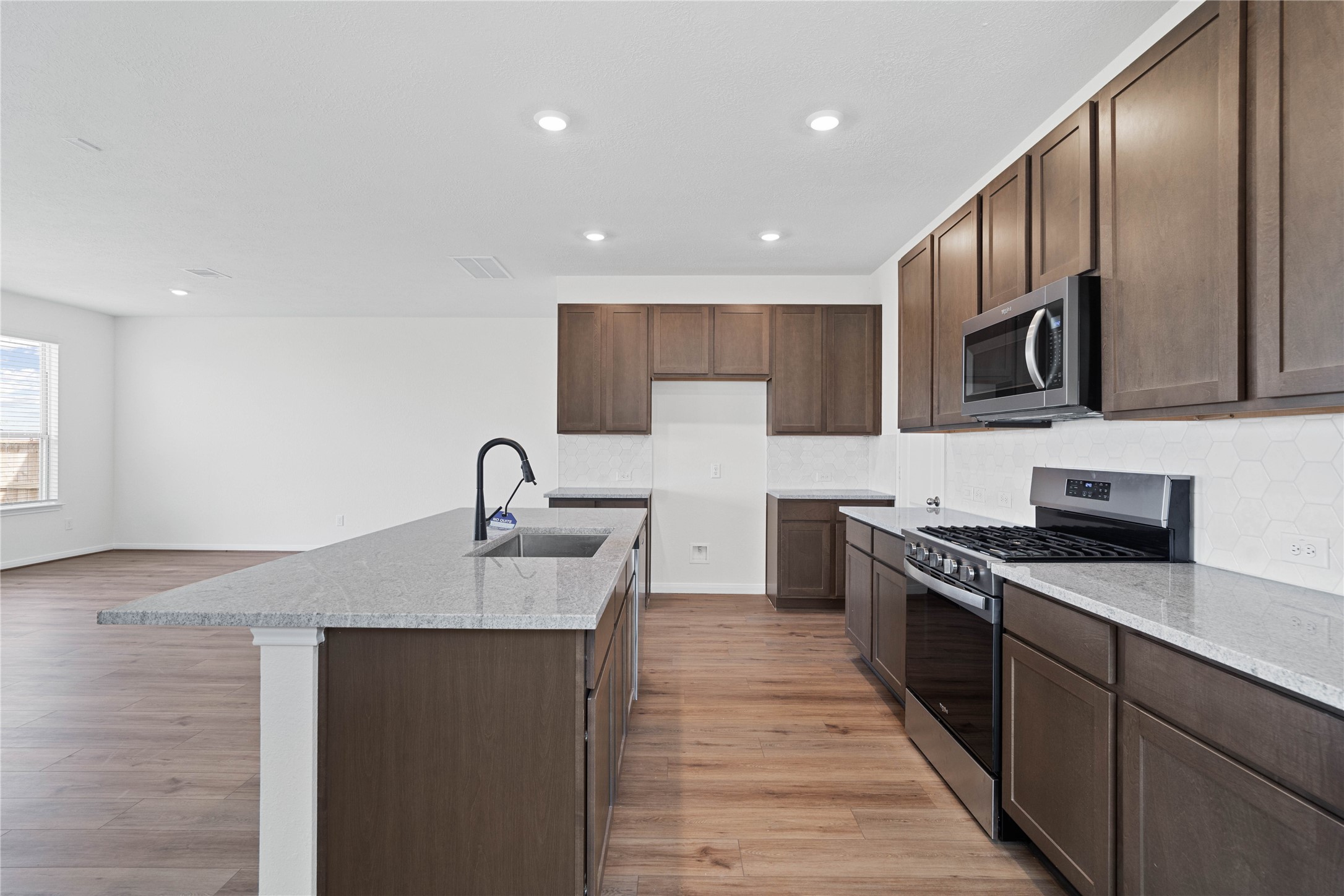 6418 Kentfield Drive Rosharon, TX 77583 - Photo 6 of 23 This spacious kitchen boasts soaring ceilings, Woodmont Dakota Shaker cabinets in a Smolder stain, Granite Summit White countertops, stainless steel Whirlpool appliances, a modern Daltile backsplash, recessed lighting, an extended breakfast bar countertop, and a pantry—all overlooking the expansive Great Room.
