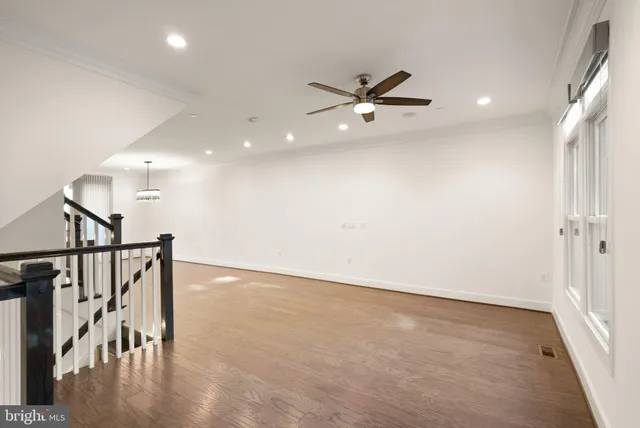 a view of an empty room with wooden floor and a ceiling fan