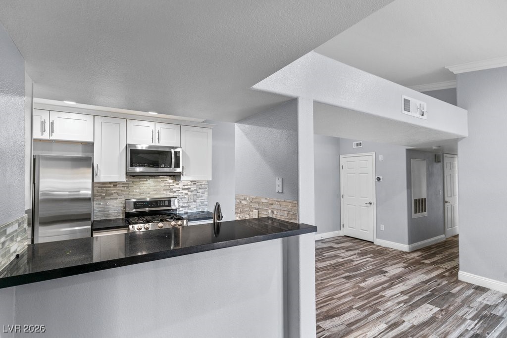7885 West Flamingo Road, Unit 1053 Las Vegas, NV 89147 - Photo 7 of 33 Kitchen featuring stainless steel appliances, tasteful backsplash, white cabinets, dark stone countertops, and dark wood-style floors