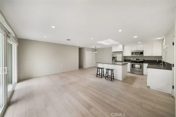 a kitchen with stainless steel appliances kitchen island granite countertop a stove a sink a refrigerator and white cabinets with wooden floor