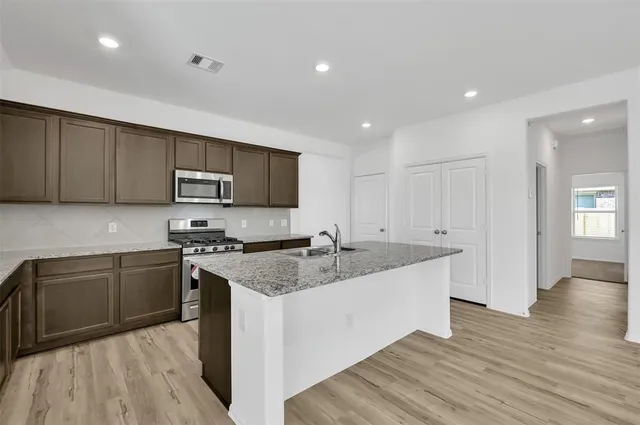 a kitchen with stainless steel appliances granite countertop wooden cabinets a sink a stove a refrigerator and dishwasher with wooden floor