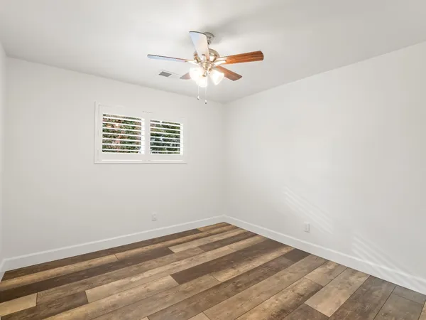 an empty room with wooden floor and ceiling fan