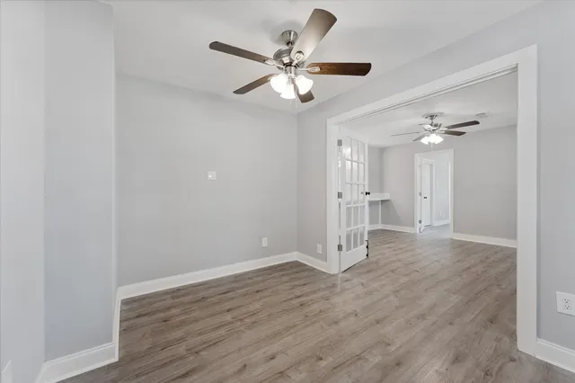 a view of an empty room with wooden floor and a ceiling fan