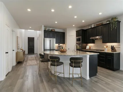 a kitchen with stainless steel appliances kitchen island granite countertop a stove top oven a sink a refrigerator and white cabinets with wooden floor