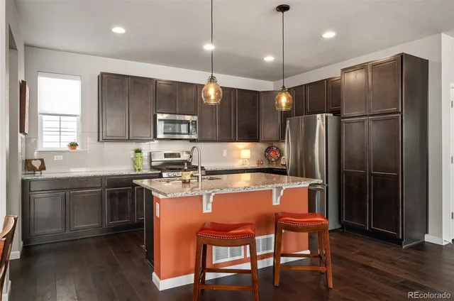 a kitchen with stainless steel appliances granite countertop a stove refrigerator a sink dishwasher a dining table and chairs with wooden floor