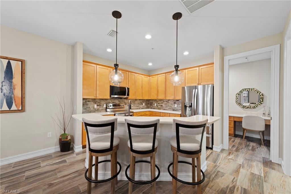 9076 Rialto Street, Unit 6204 Naples, FL 34113 - Photo 11 of 50 Kitchen featuring wood-finish cabinetry, stainless steel appliances, a tile backsplash, and a breakfast bar with pendant lighting. NEW KITCHEN LG-IQ APPLIANCES (2024), NEW QUARTZ COUNTERS (2018), NEW BACKSPLASH (2018), NEW TILE FLOOR (2018)