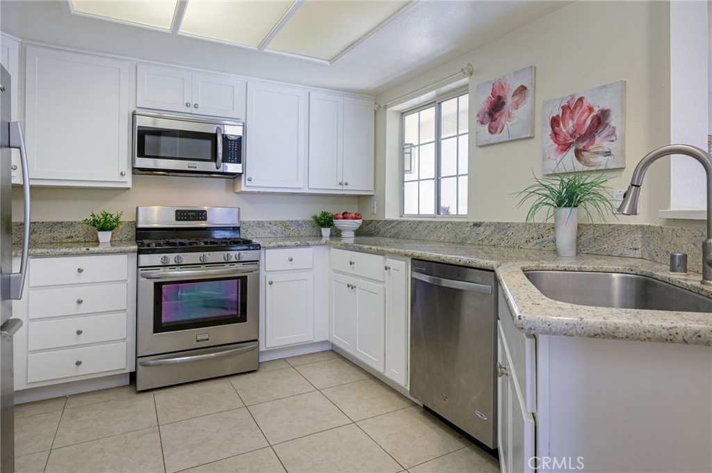 a kitchen with granite countertop white cabinets stainless steel appliances and a window