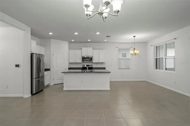 a kitchen with stainless steel appliances kitchen island granite countertop a refrigerator a stove a sink and white cabinets with wooden floor