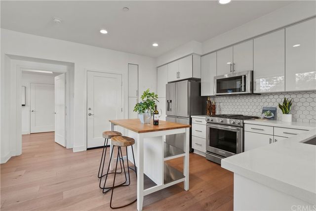 a kitchen with stainless steel appliances a stove a sink dishwasher a refrigerator and a dining table with wooden floor