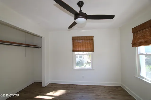 an empty room with wooden floor cabinet and windows