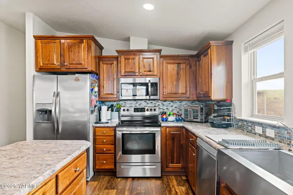 a kitchen with stainless steel appliances granite countertop wooden cabinets a sink dishwasher a stove and a refrigerator with wooden floor