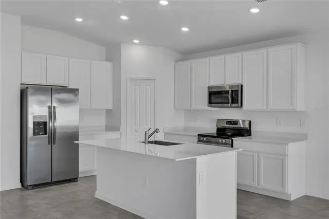 a kitchen with stainless steel appliances granite countertop a refrigerator a stove a sink and white cabinets