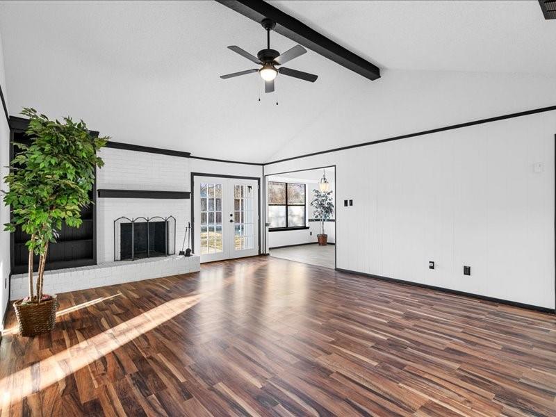 3977 Windhaven Road Fort Worth, TX 76133 - Photo 7 of 23 Vaulted ceiling with exposed beams, wood-finish flooring, white brick fireplace, built-in shelving, and double French doors