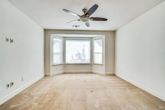 an empty room with ceiling fan and windows