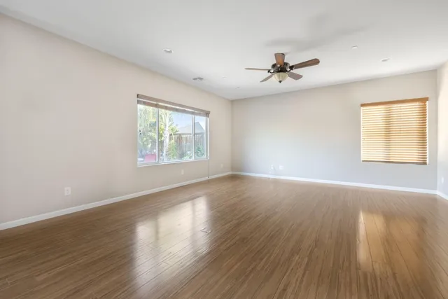 an empty room with wooden floor ceiling fan and windows