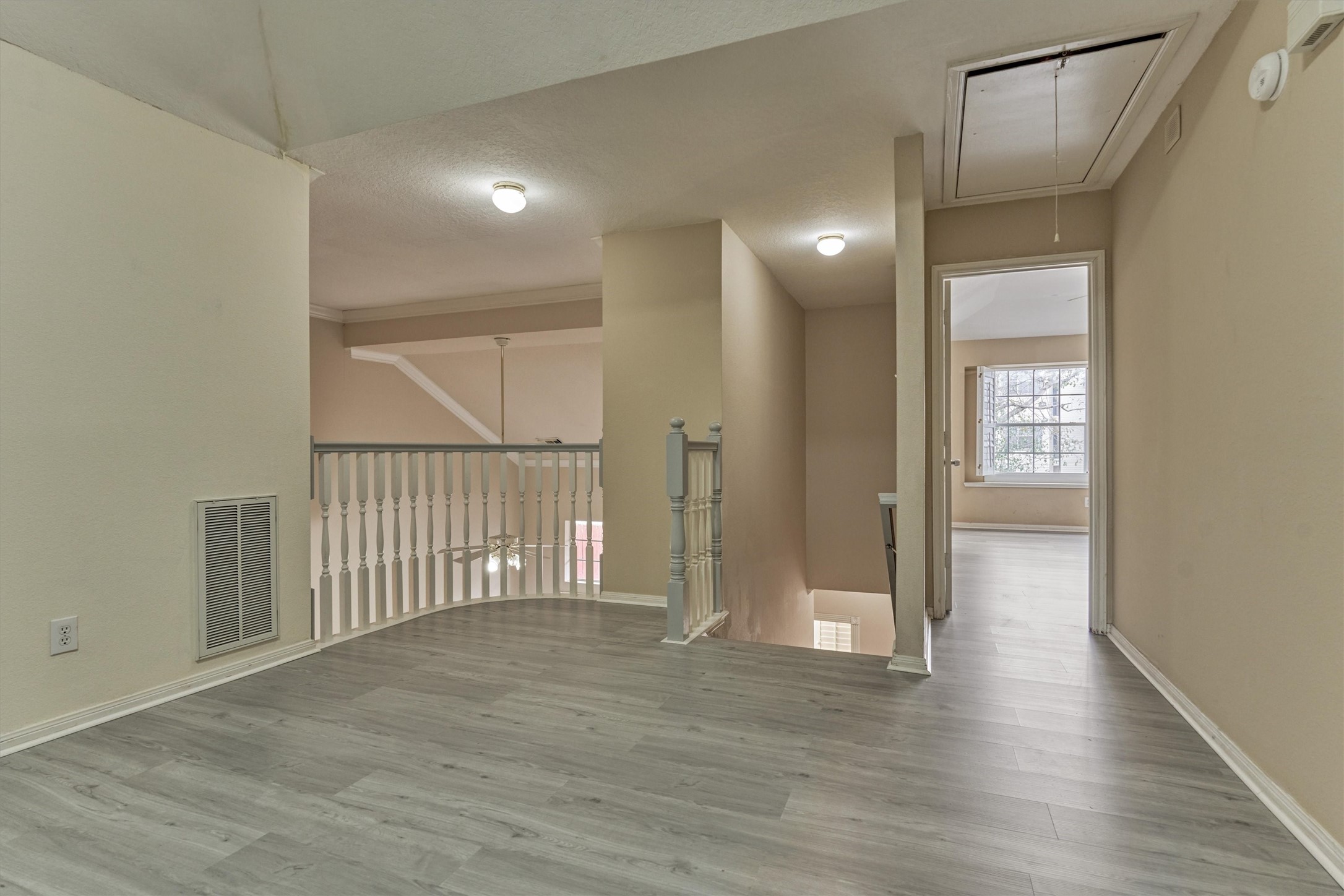 14420 Walters Road, Unit 26 Houston, TX 77014 - Photo 26 of 45 This photo shows a bright, open hallway with light wood-look flooring and neutral walls. It features a railing overlooking a lower level and a door leading to the primary bedroom with a large window, providing plenty of natural light.