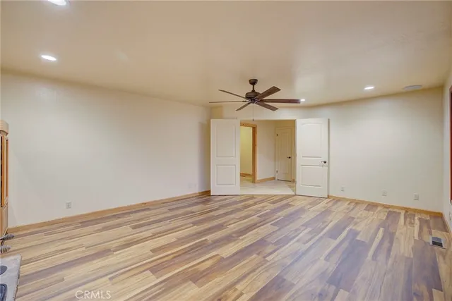 an empty room with wooden floor fan and windows