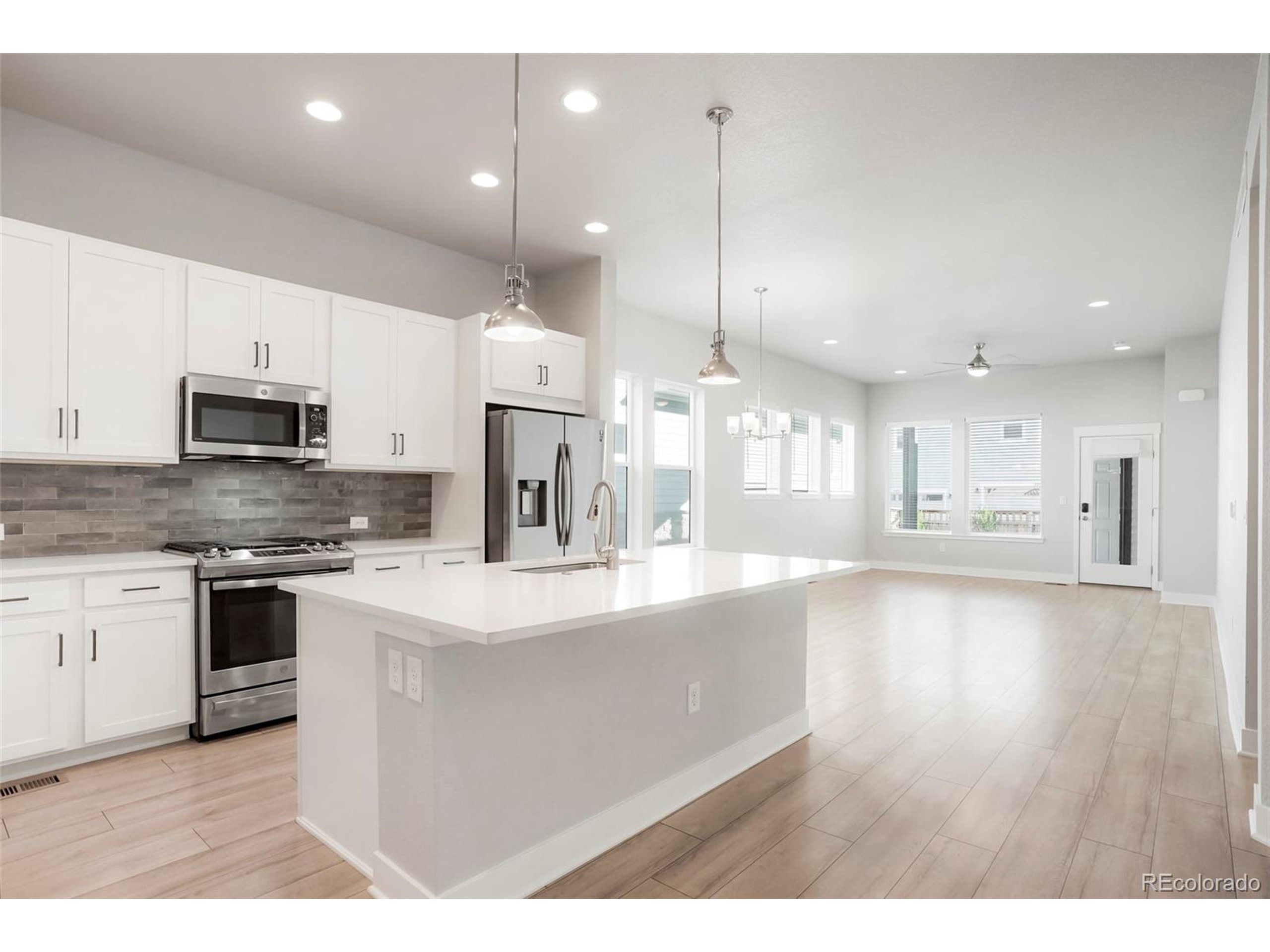 20968 East 60th Place Aurora, CO 80019 - Photo 2 of 50 a large kitchen with stainless steel appliances kitchen island granite countertop a stove a sink a refrigerator and white cabinets with wooden floor