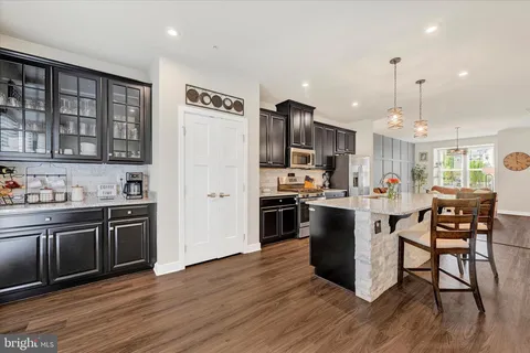 a kitchen with stainless steel appliances kitchen island granite countertop a refrigerator a stove top oven a sink dishwasher and white cabinets with wooden floor next to windows