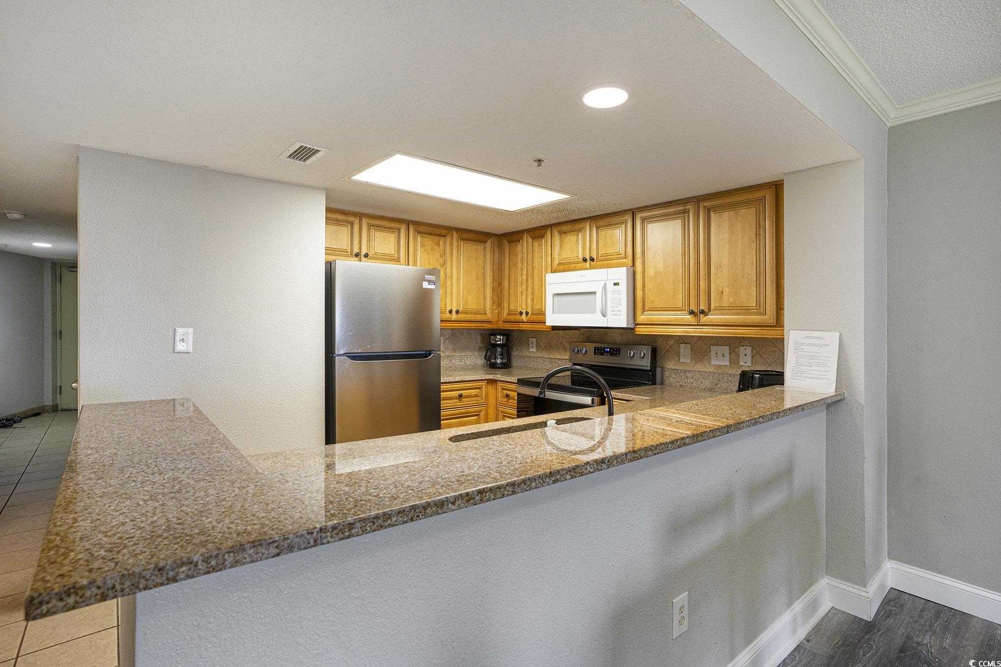 7100 North Ocean Boulevard, Unit 320 Myrtle Beach, SC 29572 - Photo 10 of 40 Kitchen with tasteful backsplash, light stone countertops, appliances with stainless steel finishes, ornamental molding, and brown cabinets