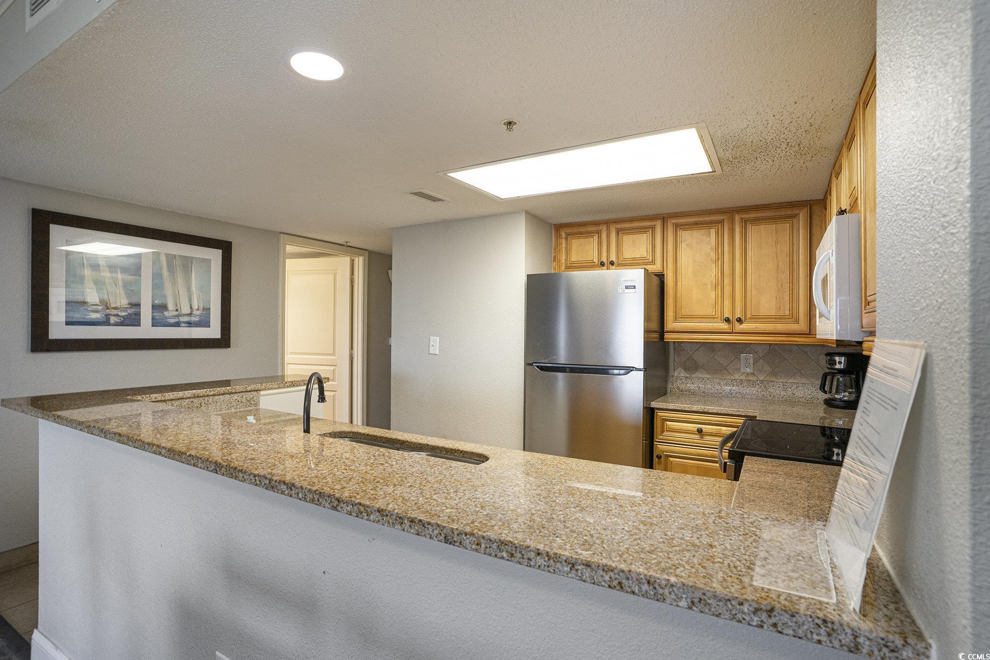 7100 North Ocean Boulevard, Unit 320 Myrtle Beach, SC 29572 - Photo 11 of 40 Kitchen featuring freestanding refrigerator, light stone counters, backsplash, a peninsula, and electric range oven