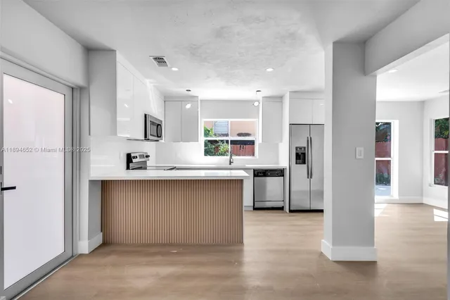 a large white kitchen with stainless steel appliances granite countertop a refrigerator and a sink