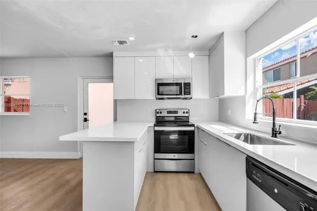 a kitchen with stainless steel appliances a sink dishwasher a stove top oven a refrigerator with wooden floor and cabinets