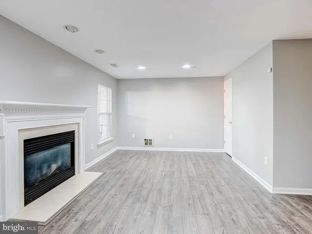 a view of an empty room with wooden floor fireplace and a window