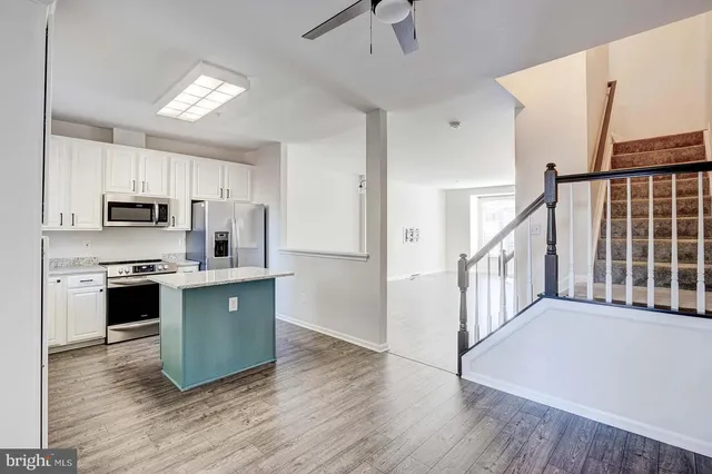 a kitchen with stainless steel appliances granite countertop a refrigerator a stove top oven a sink dishwasher and white cabinets with wooden floor