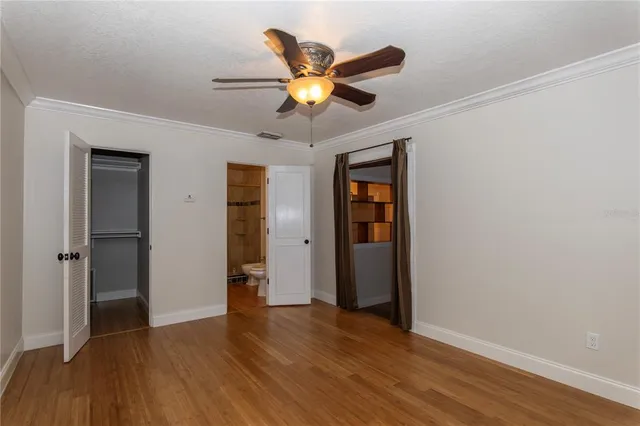 a view of an empty room with wooden floor and a ceiling fan